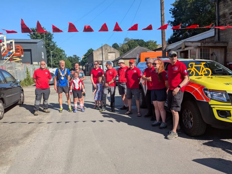 Group of Rescue volunteers celebrating Winnie completing her adventure, with red flags and vehicles in the background.