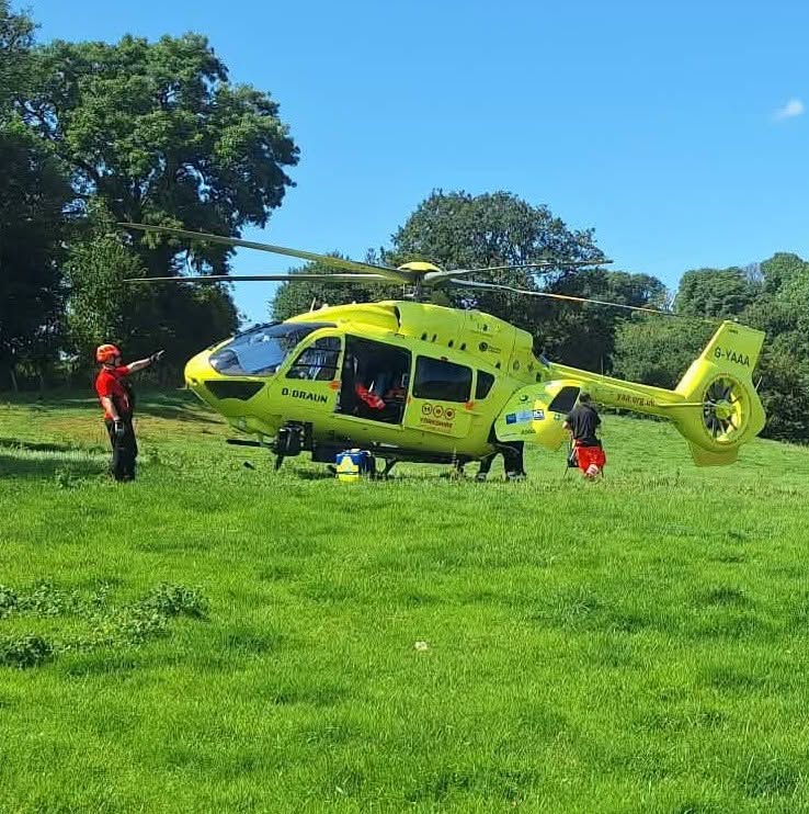 A yellow emergency helicopter on a grassy field with rescue personnel preparing for a mission under a clear blue sky.